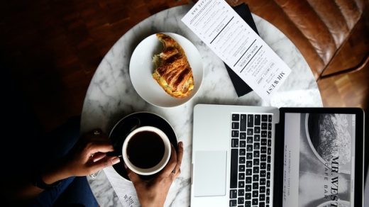kopi hitam diletakkan diatas meja dengan laptop dan croissant