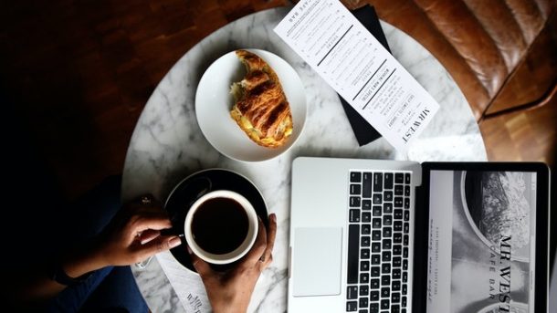 kopi hitam diletakkan diatas meja dengan laptop dan croissant